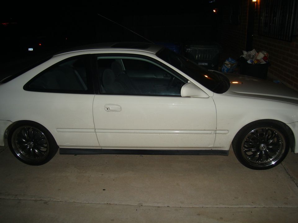 Side view of a white coupe with aftermarket rims parked on a concrete surface