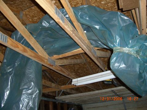 1993 Ford Probe - Attic space with insulation covered by blue plastic sheeting, showing wooden roof trusses and a fluorescent light fixture.