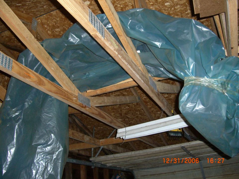 Attic with blue plastic sheeting covering insulation and wooden beams
