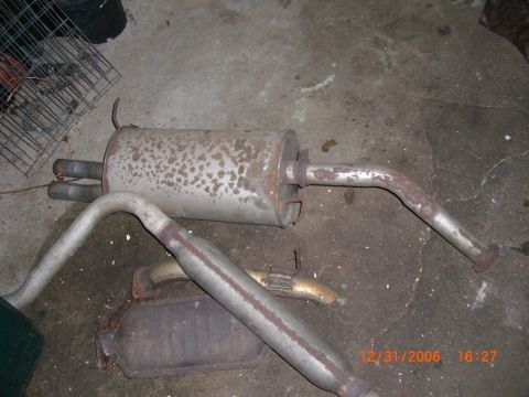 1993 Ford Probe - Rusty exhaust system parts, including mufflers and pipes, lie on a concrete surface.