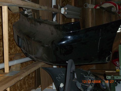1993 Ford Probe - A black car bumper is stored on shelves, showing signs of wear and tear.