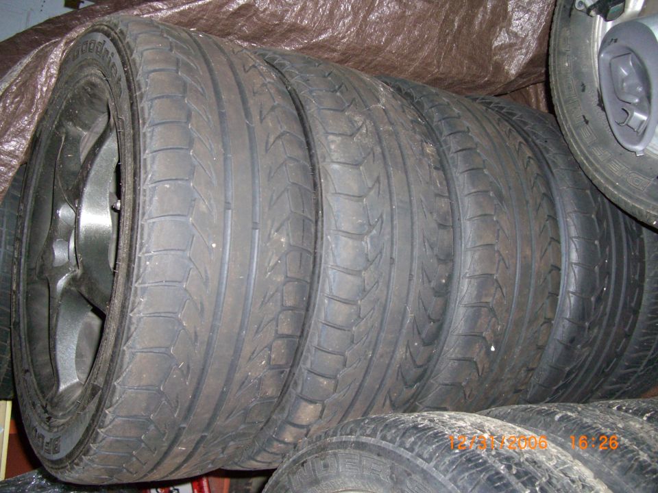 Stack of four used tires with black rims, one tire visible on the right