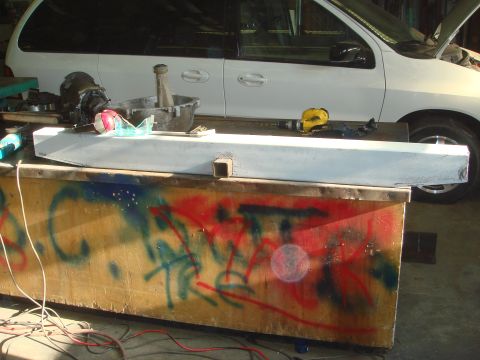 1996 Ford Bronco - A white minivan is parked in a workshop, its hood open, with a white bumper part resting on a table in front of it.