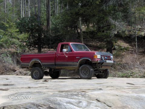 1990 Ford F-150 - This lifted red Ford F-150 is parked on a rocky surface with trees in the background.