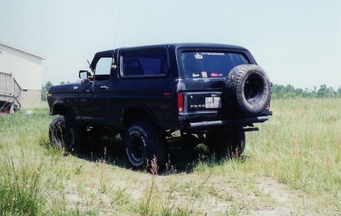 1978 Ford Bronco - Rear view of a black 1978 Ford Bronco parked in a grassy field with a spare tire on the tailgate.