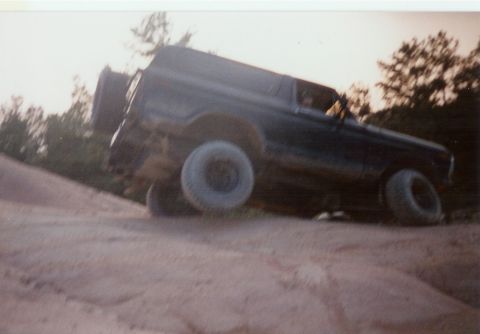 1978 Ford Bronco - A dark 1978 Ford Bronco navigates a steep dirt incline, its off-road capabilities.
