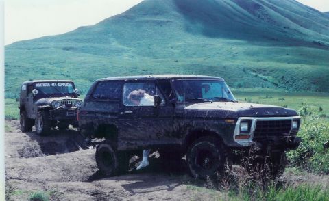1978 Ford Bronco - Two off-road vehicles navigate a muddy path, with a Jeep following a Ford Bronco up a hill.