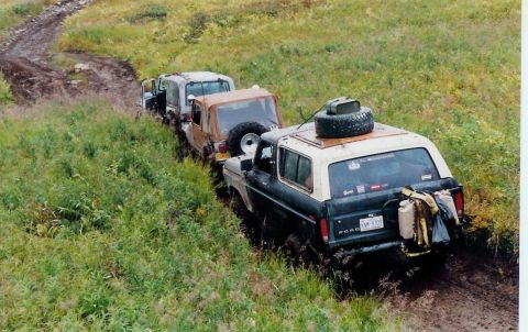 1978 Ford Bronco - Several off-road vehicles are navigating a muddy trail, with the lead vehicle appearing to be a 1978 Ford Bronco.