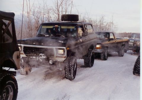 1978 Ford Bronco - Several off-road vehicles are driving in a snowy landscape, kicking up snow.