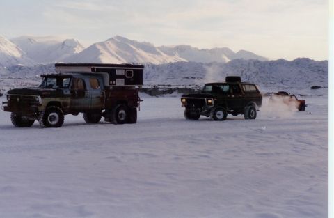 1978 Ford Bronco - Two trucks traverse a snowy terrain with mountains in the background.