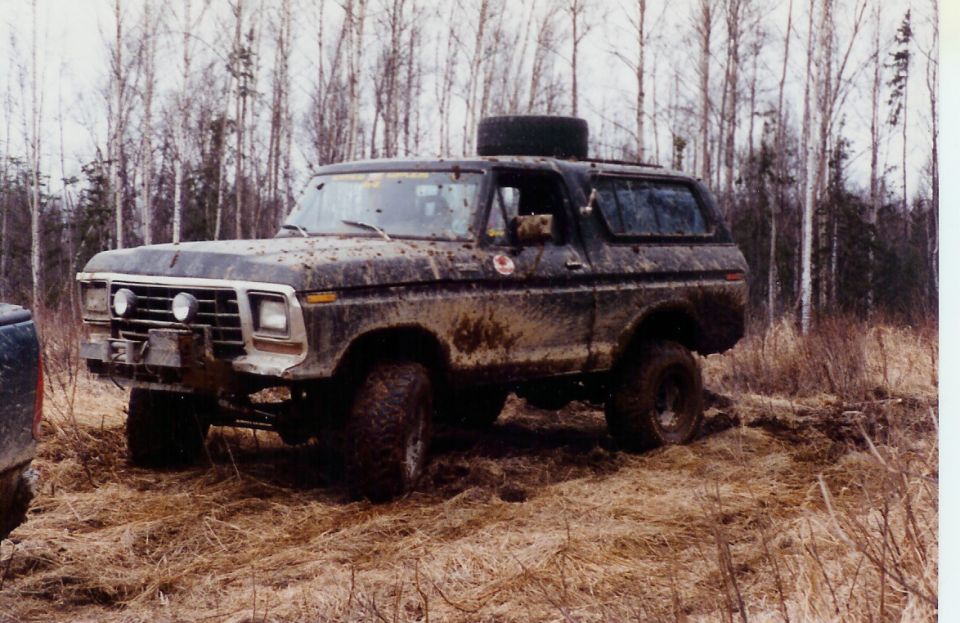 Muddy 1978 Ford Bronco parked in a wooded area with a spare tire on the roof