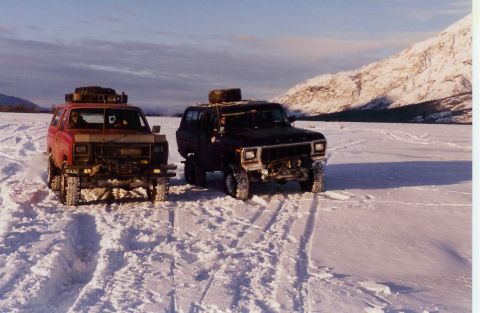1978 Ford Bronco - Two 1978 Ford Broncos equipped for off-road travel sit in a snowy, mountainous terrain under a partly cloudy sky.