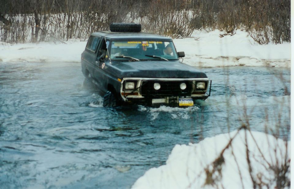 1978 Ford Bronco driving through a shallow river in winter