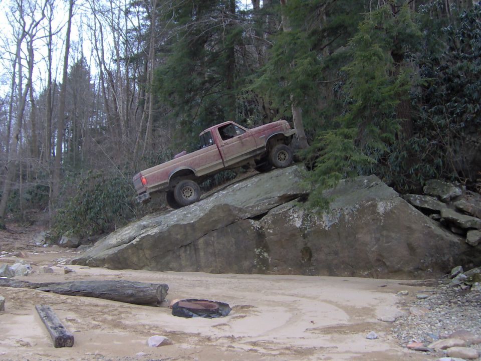 Red 1990 Ford F-150 climbing large rocks off-road