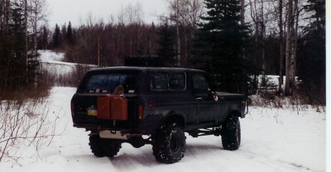 1978 Ford Bronco - 1978 Ford Bronco equipped with auxiliary gas cans, parked on a snow-covered trail in a wooded area.