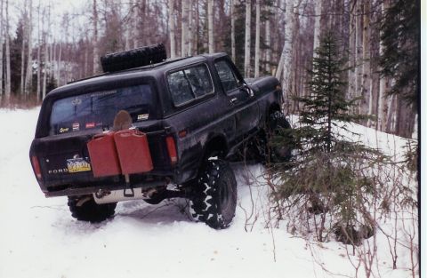 1978 Ford Bronco - A black 1978 Ford Bronco navigates a snowy, wooded terrain with auxiliary fuel cans and a shovel attached.
