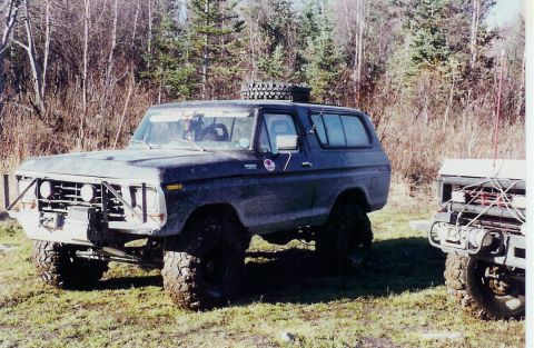 1978 Ford Bronco - A modified 1978 Ford Bronco sits in a grassy, wooded area next to another off-road vehicle.