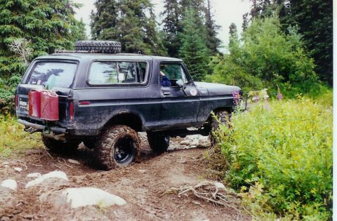 1978 Ford Bronco - This 1978 Ford Bronco navigates a , wooded trail, equipped for an off-road adventure with extra fuel and a spare tire.