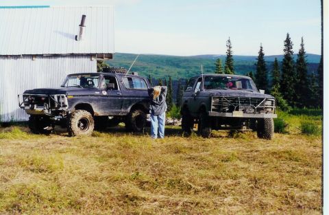 1978 Ford Bronco - Two off-road modified Ford Broncos are parked outside a building with a scenic mountain backdrop.