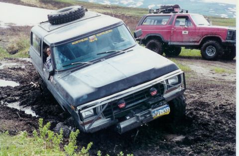 1978 Ford Bronco - Two off-road vehicles are stuck in thick mud on a trail, with one vehicle's front end angled down.