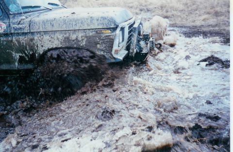 1978 Ford Bronco - This 1978 Ford Bronco is navigating a challenging muddy terrain, kicking up significant spray.