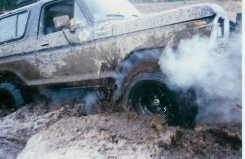 1978 Ford Bronco - A 1978 Ford Bronco struggles through deep mud, its front tire spinning and spraying dirt.