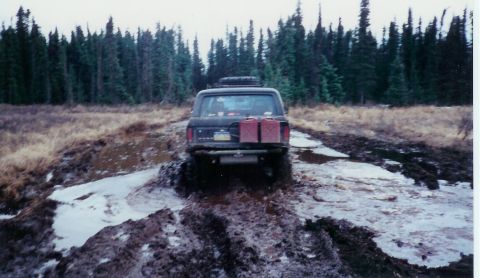 1978 Ford Bronco - A 1978 Ford Bronco navigates a challenging muddy and icy trail, equipped with auxiliary fuel cans for extended travel.