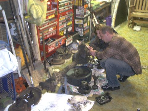 1986 Ford Bronco - Two people examine a vehicle differential and its components laid out on the floor of a cluttered garage.