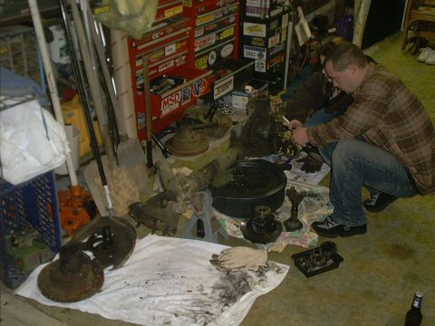 1986 Ford Bronco - A mechanic works on differential gears spread out on a shop floor, surrounded by tools and other vehicle parts.