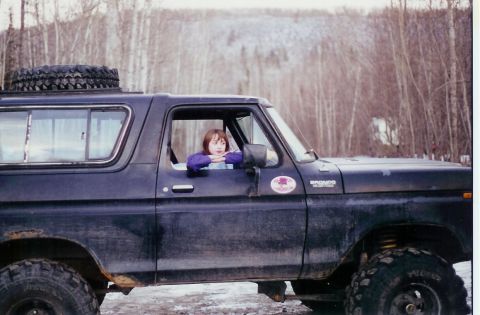 1978 Ford Bronco - Side view of a 1978 Ford Bronco parked in a snowy, wooded landscape with a person inside.