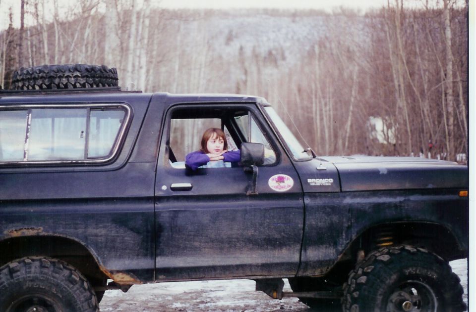 1978 Ford Bronco with a person looking out the driver's window, spare tire on roof, in a wooded area