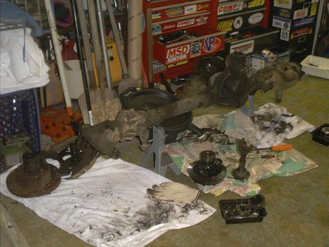1986 Ford Bronco - A disassembled front axle assembly lies on a cloth, surrounded by tools and gears, in a garage setting.
