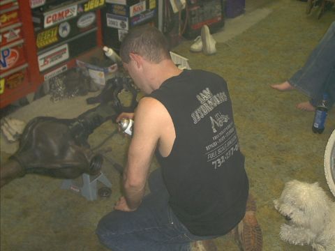 1986 Ford Bronco - A man sprays a rear axle assembly that is supported by jack stands in a garage setting.