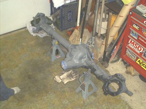 1986 Ford Bronco - A differential axle assembly is shown on jack stands in a garage setting, with tools and a toolbox visible in the background.