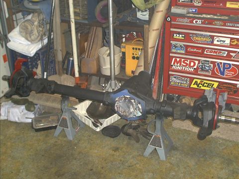 1986 Ford Bronco - A vehicle axle assembly is shown supported by jack stands in a cluttered garage setting.