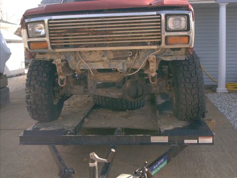1986 Ford Bronco - This Ford Bronco is on a lift, revealing its front end with a prominent grille and large tires.