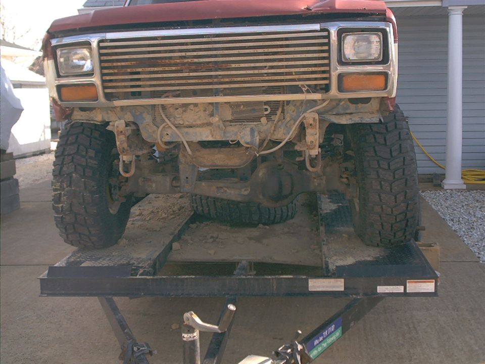Front of a red Ford Bronco on a lift, showing the grille, headlights, and front tires