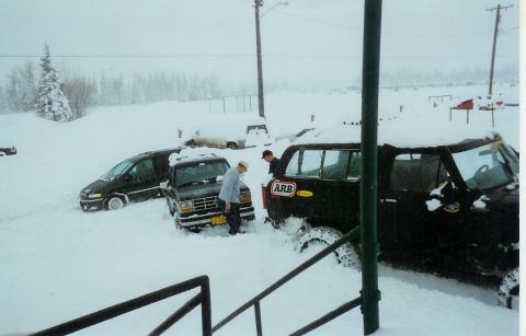 1978 Ford Bronco - Multiple vehicles are buried in snow, with two individuals assessing the situation near a black SUV.