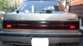1997 Ford Crown Victoria - The rear of a silver Acura Vigor is shown, its V6 badging and a dark horizontal trim piece connecting the taillights.