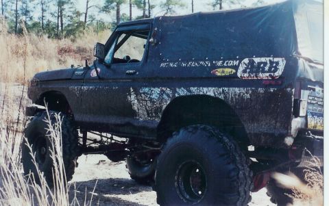 1978 Ford Bronco - A heavily muddied 1978 Ford Bronco is shown off-road with a canvas top and various decals on its side.
