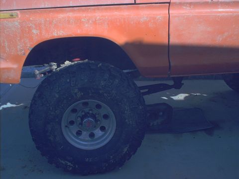 1978 Ford Bronco - The orange paint on this vehicle is dirty and shows some wear. The tire is large and appears to be for off-road use.