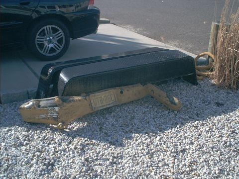 1978 Ford Bronco - A trailer hitch and frame are resting on gravel, with a black car parked nearby.