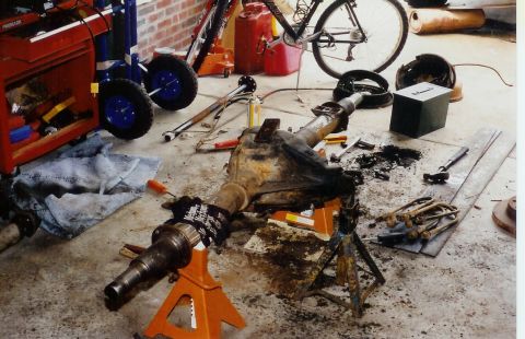 1978 Ford Bronco - A disassembled differential axle assembly rests on jack stands amidst tools and garage clutter.