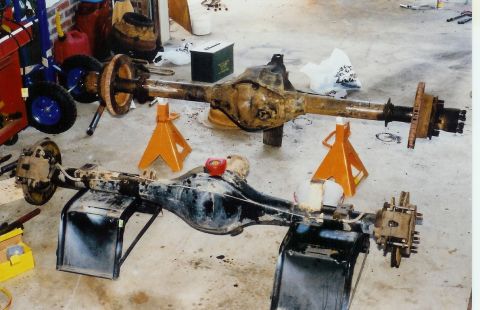 1978 Ford Bronco - Two vehicle axles, likely for a truck or SUV, are shown disassembled and resting on orange jack stands in a garage setting.