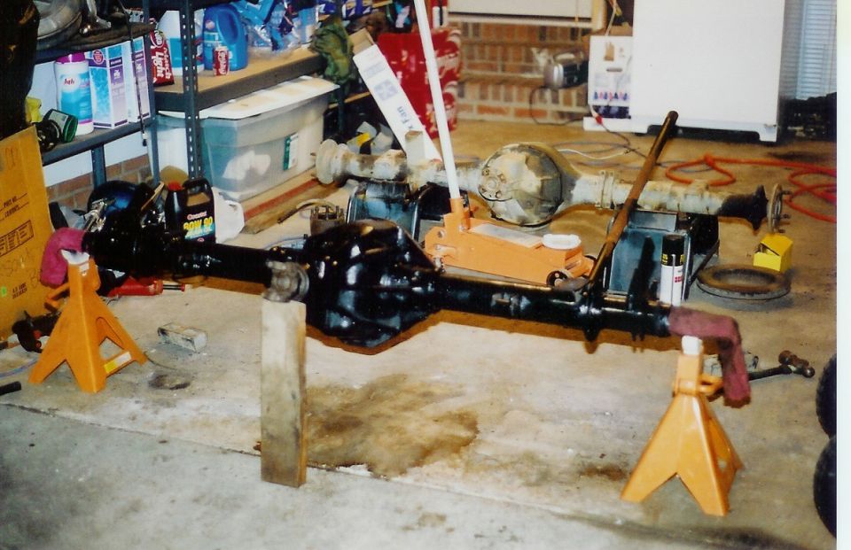 Two vehicle axles, one black and one gray, supported by jack stands in a garage