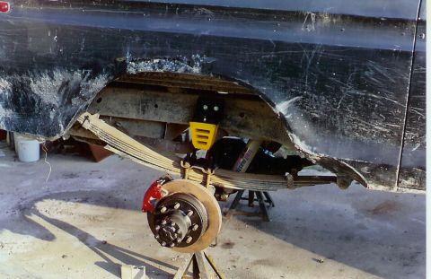 1978 Ford Bronco - Close-up view of the rear suspension and brake system, showing leaf springs, a red brake caliper, and a yellow shock mount.