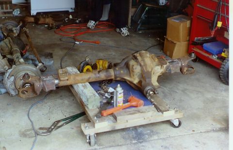 1978 Ford Bronco - A front axle assembly, likely from a truck, rests on a creeper in a garage setting.