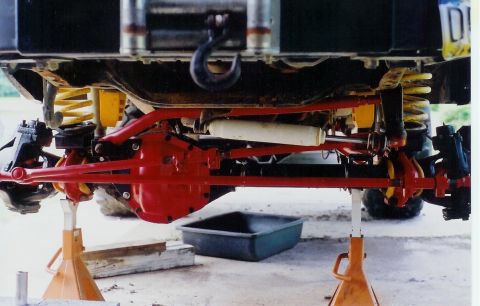1978 Ford Bronco - The underside of a vehicle is shown, lifted on jack stands with its axles and suspension system visible.