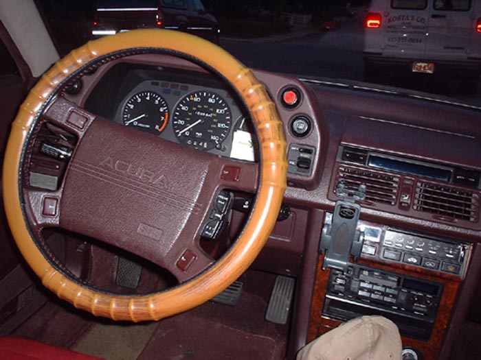 Interior shot of an Acura with a wood-rimmed steering wheel and dashboard. A van is visible outside