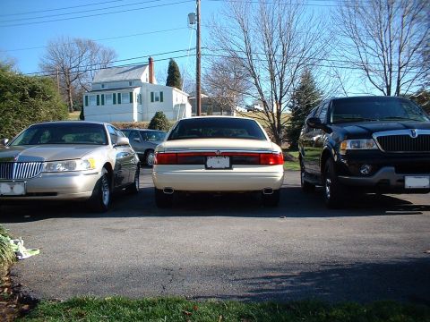 1996 Mercury Grand Marquis - A trio of vehicles are parked in a residential driveway on a sunny day.